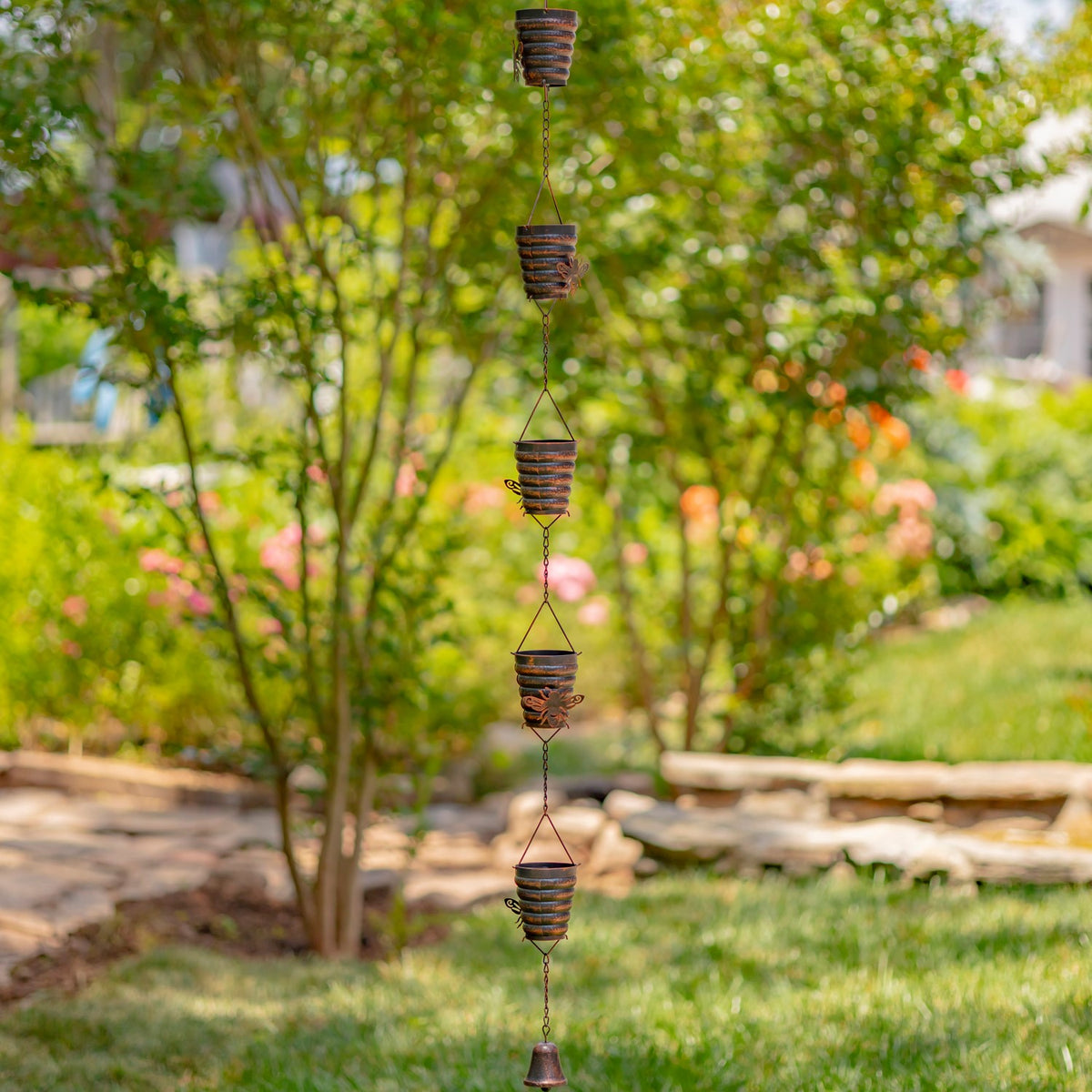 Long antique bronze rain chain hanging in a garden beside a stone path