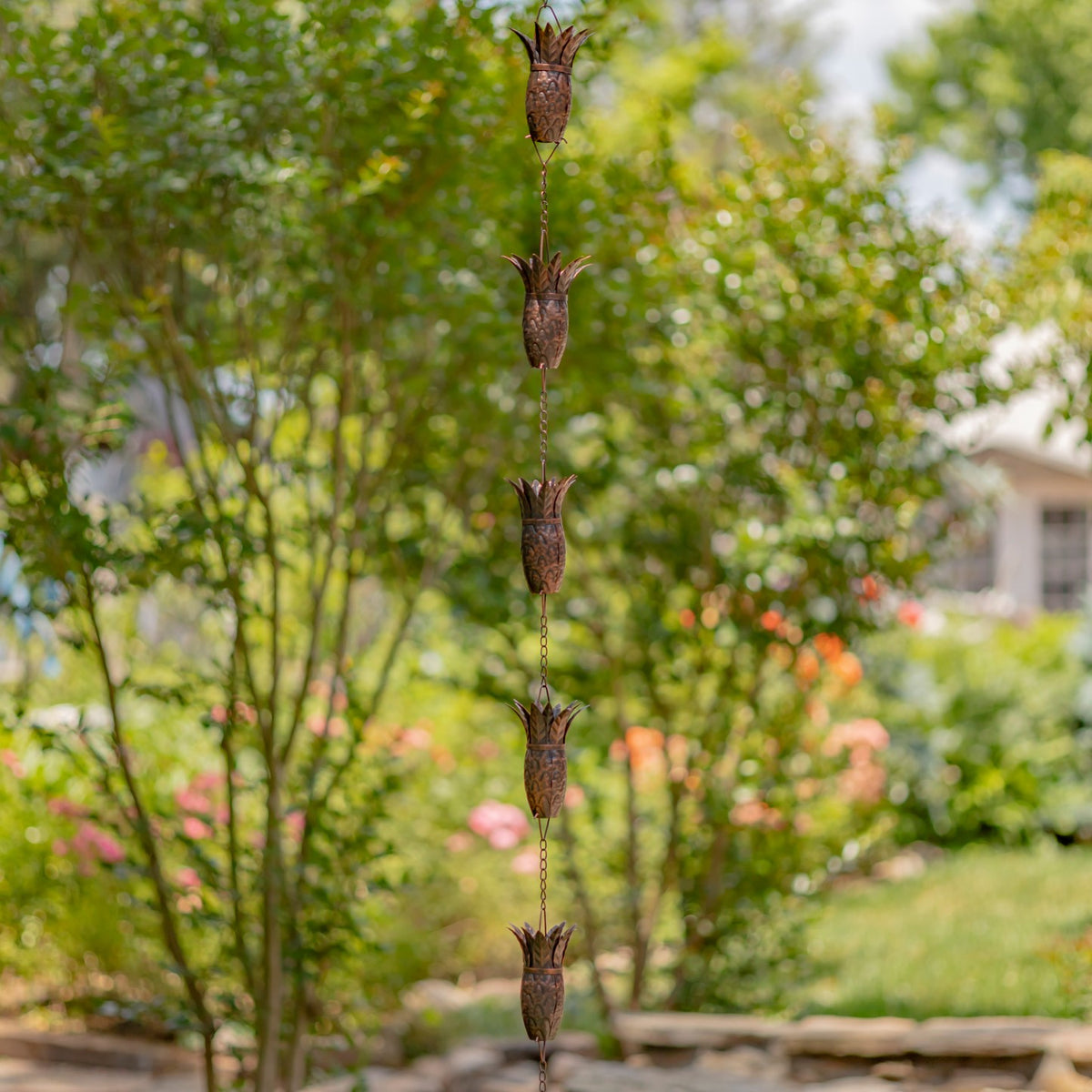 Long antique bronze rain chain with multiple pineapple-shaped links hanging in a garden