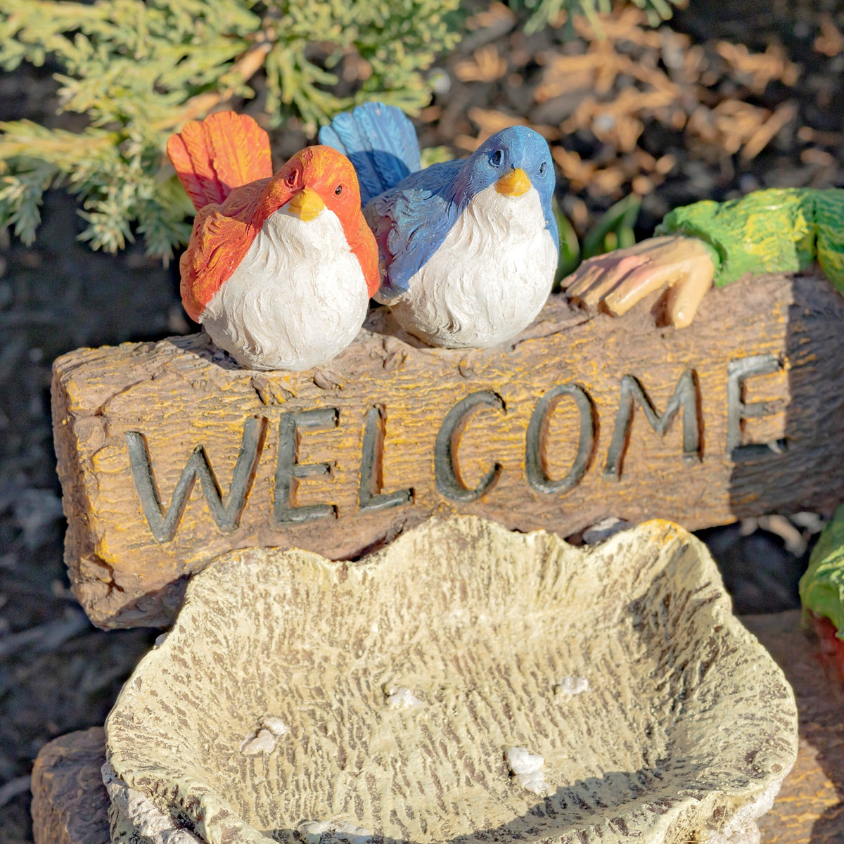 Two small painted birds perch above the carved sign, with the textured birdbath visible below.