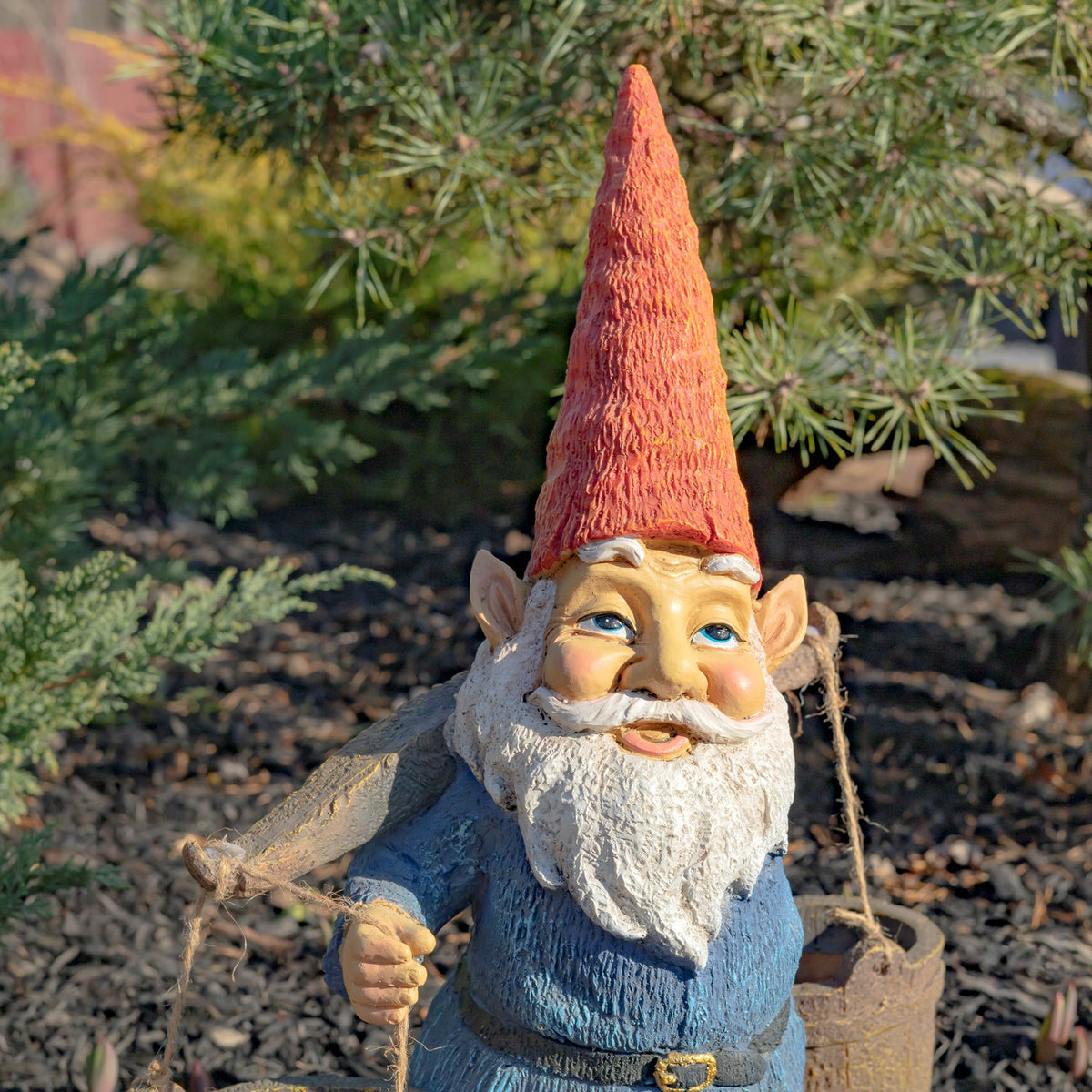 The gnome is shown against garden greenery, with one hand gripping a bucket rope.