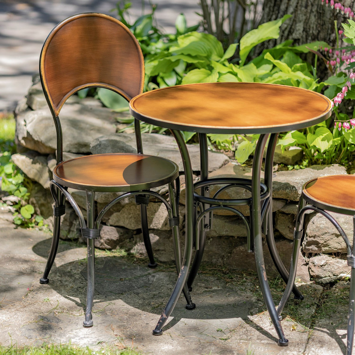Round copper bistro table and chair beside a garden stone wall