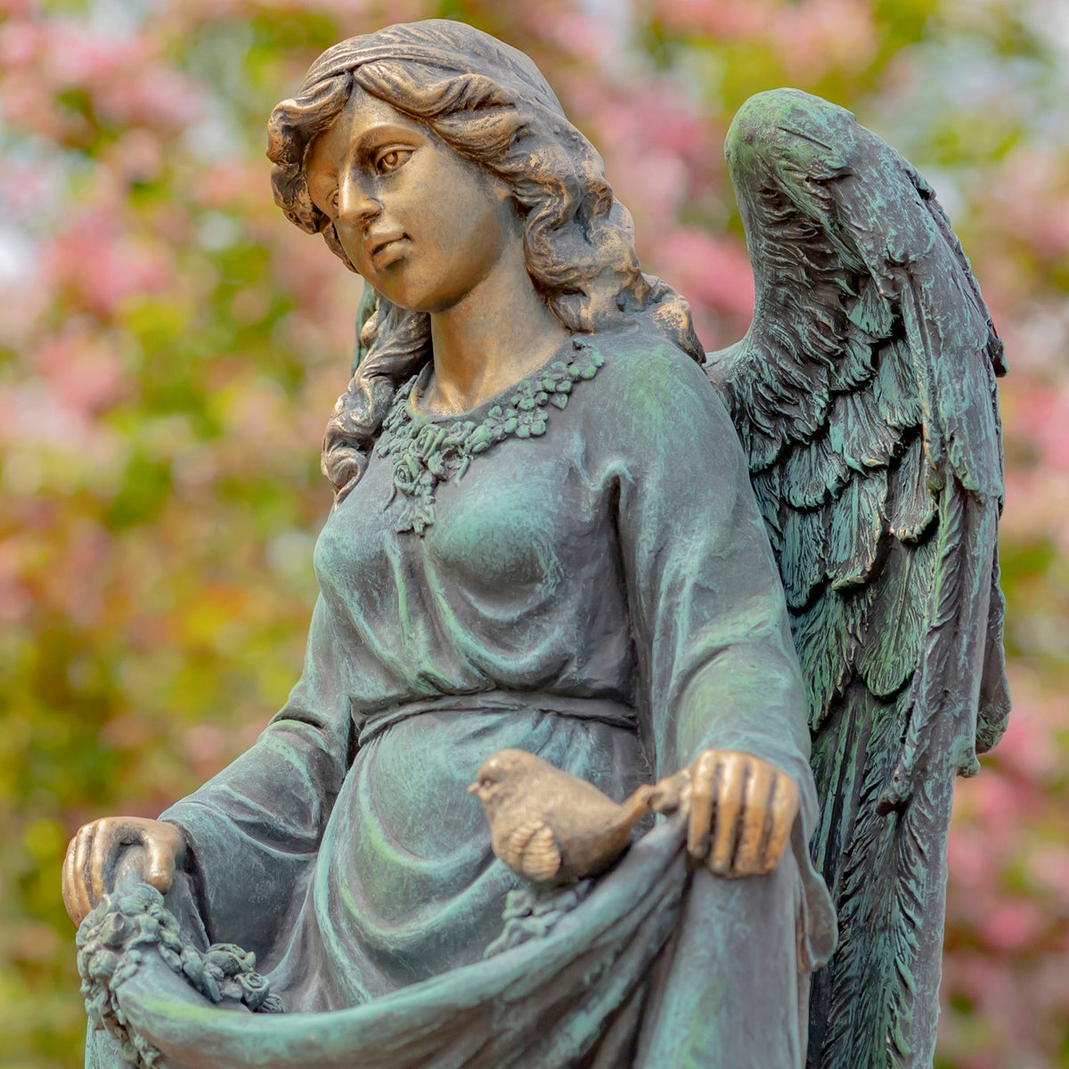 Angel statue holding up her dress, with a small bird resting on the gathered fabric.