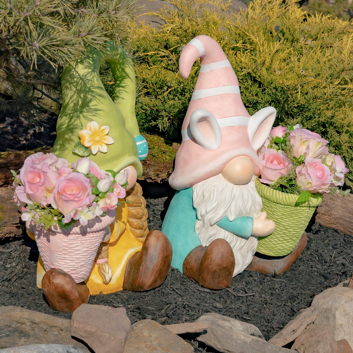 The two gnomes and their flower planters appear together in a sunlit garden bed.