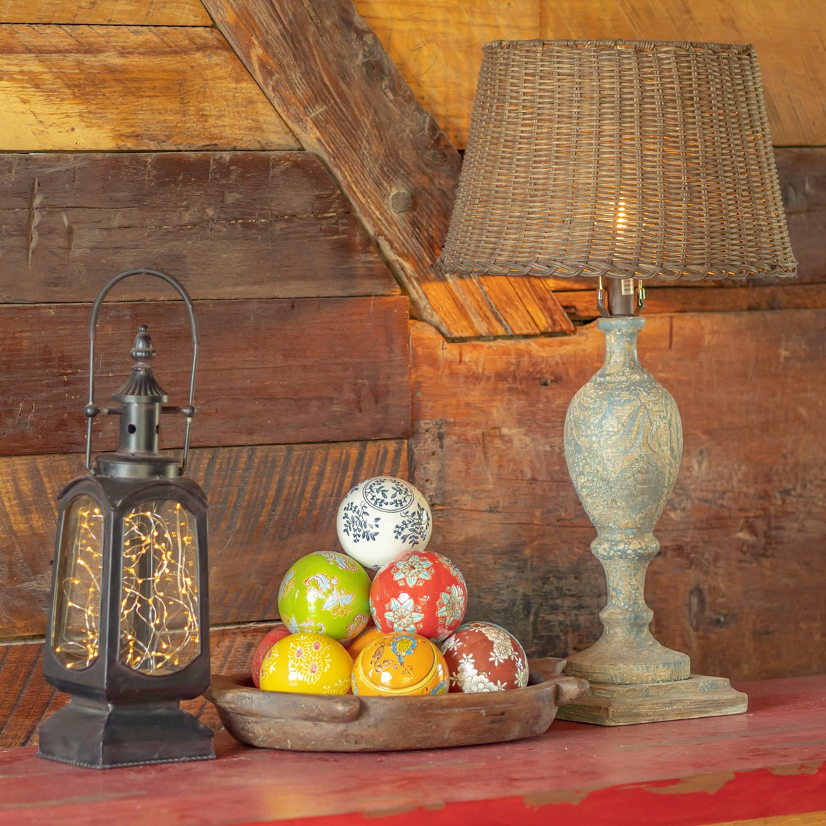 Colorful patterned ceramic balls arranged in a shallow bowl beside a lantern and a decorative table lamp.