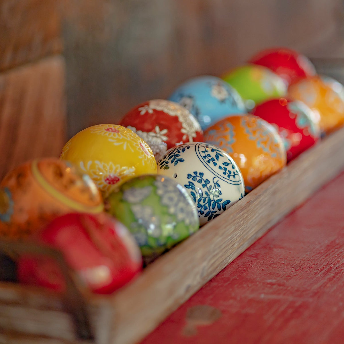 A row of glossy patterned balls in varied bright colors fills a narrow wooden tray.