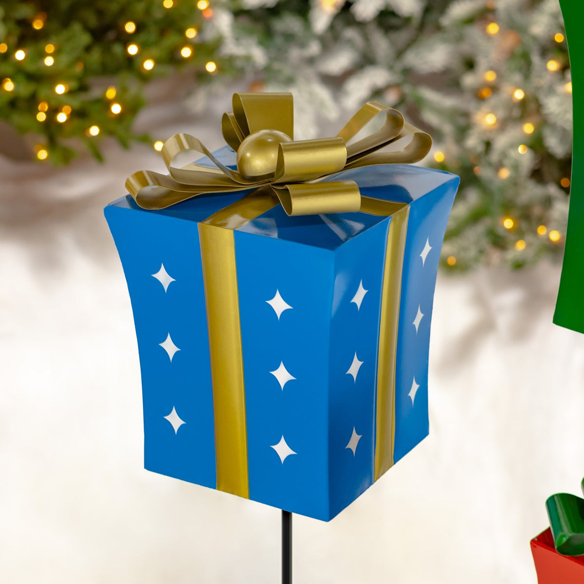 Close-up of the blue gift-box stake with a gold ribbon, bow, and white star cutouts.