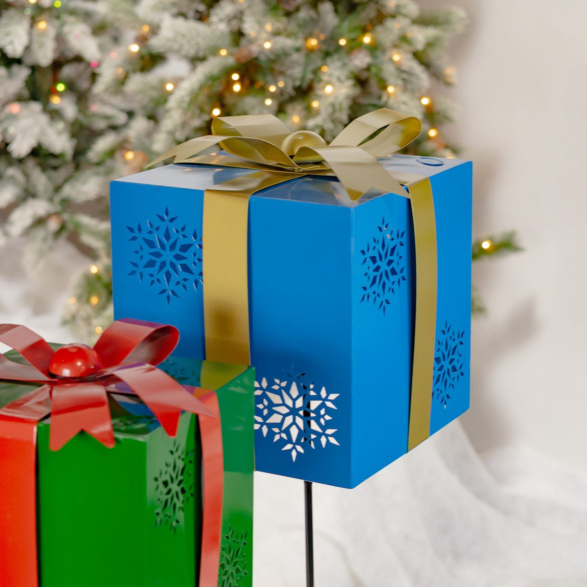 Blue gift-box garden stake with gold bow and snowflake cutouts, shown close up