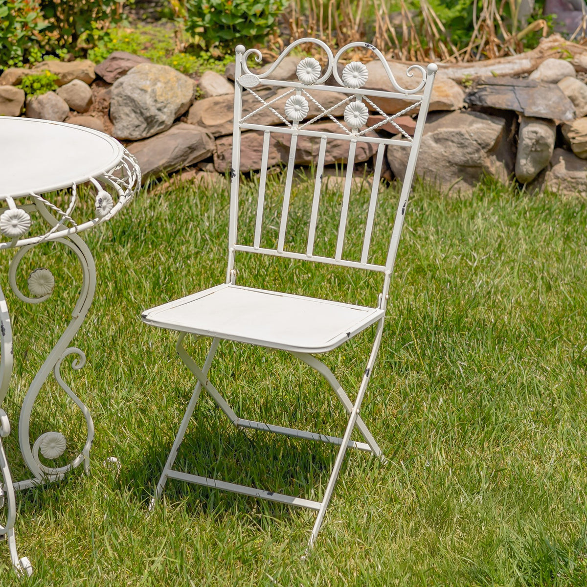 Antique white folding bistro chair with decorative flower details on a lawn