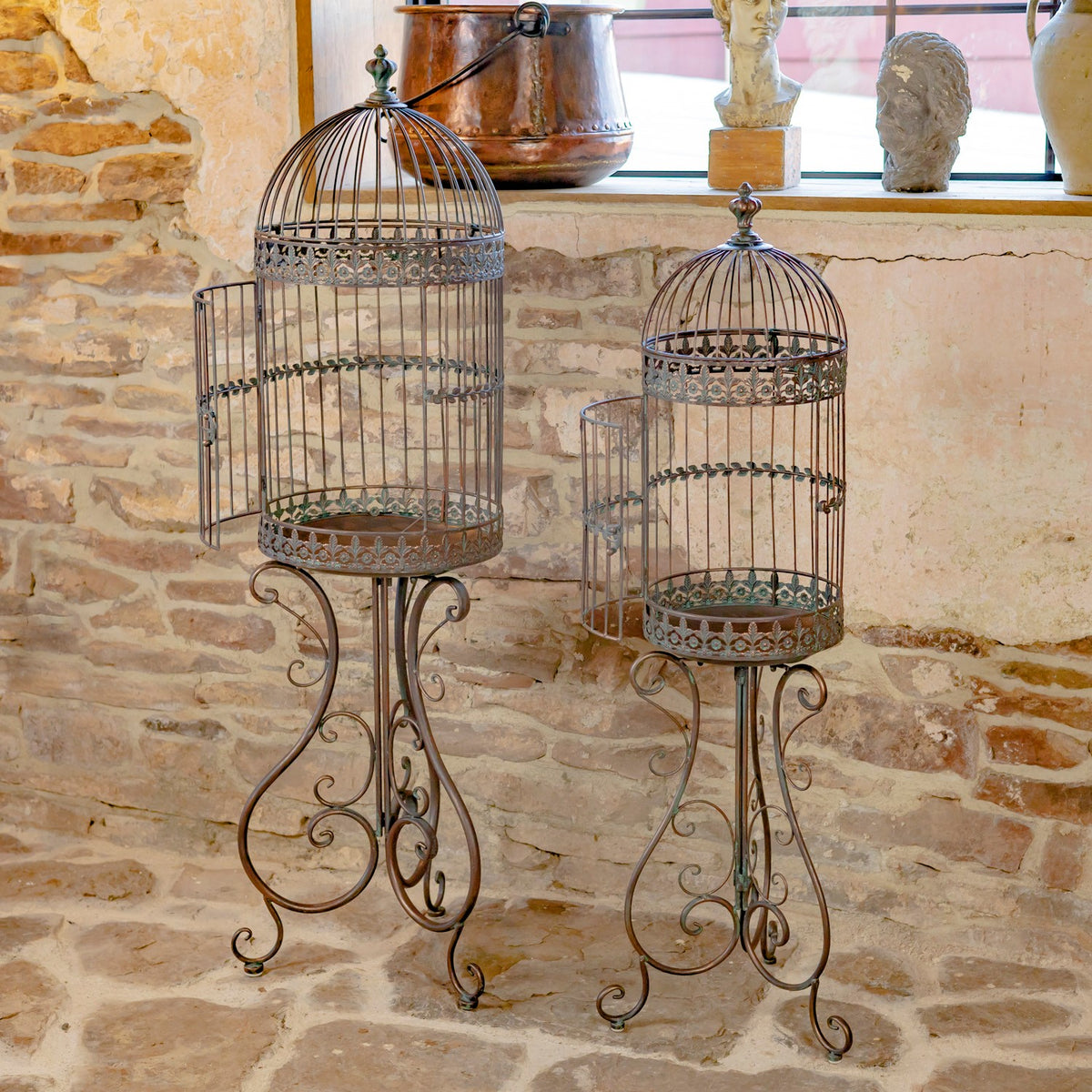 Two dark iron birdcage planters with open side doors and ornate curled stands.