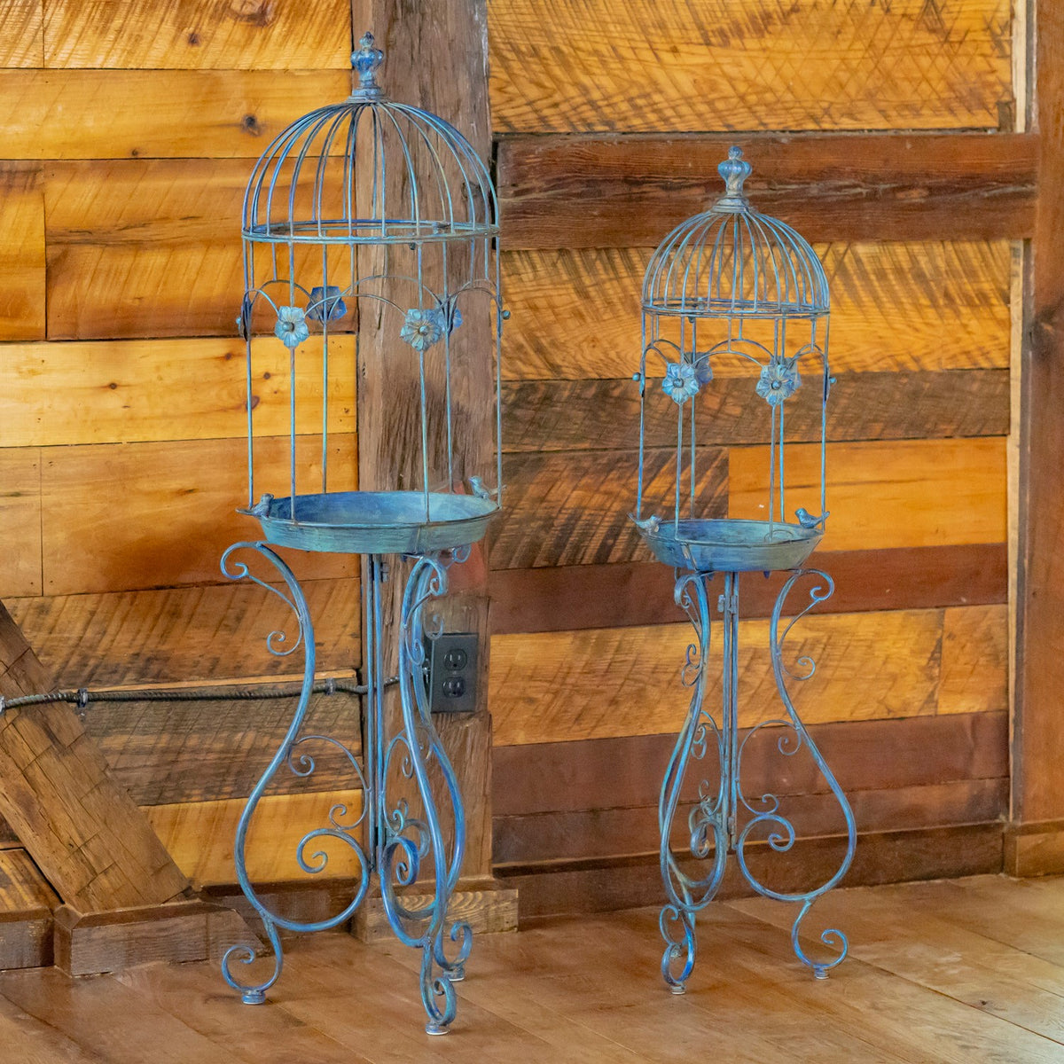 Two ornate blue birdcage planters on curled stands, shown nearly full height on a wooden floor.