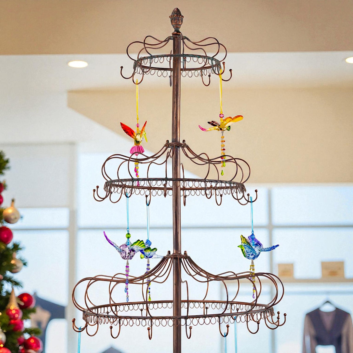 Upper tiers of the metal stand show decorative scrollwork and hooks with bright bird ornaments hanging from them.