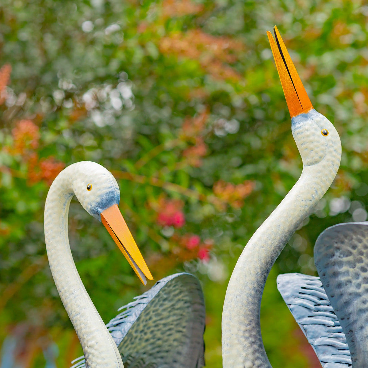 Close view of two white heron necks and orange beaks against a garden backdrop