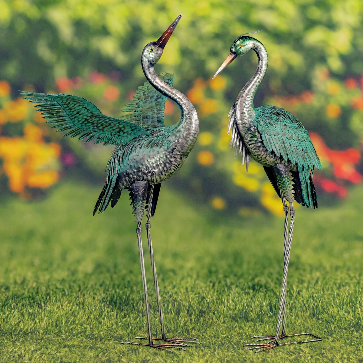 Two metal herons face each other on a lawn, one with its wing extended.