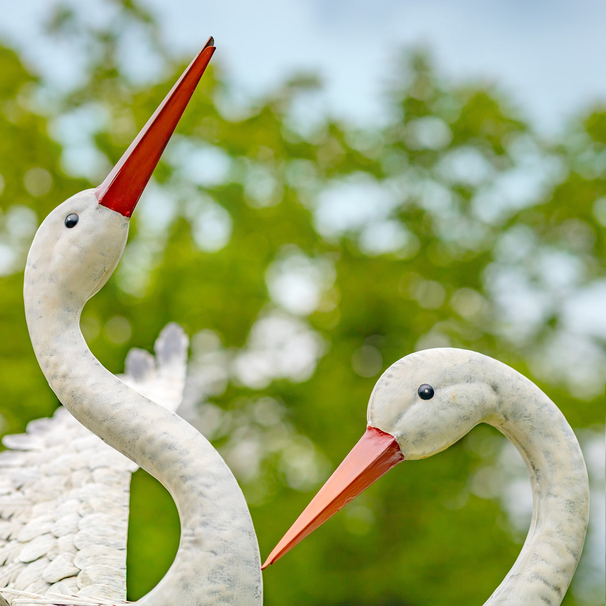 Close view of two heron statue heads, showing their curved necks and long orange beaks.