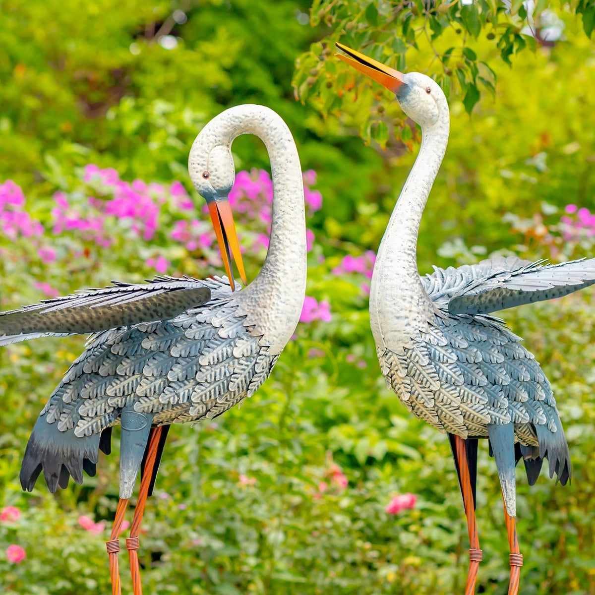 Pair of blue-and-white egret figurines viewed among garden greenery