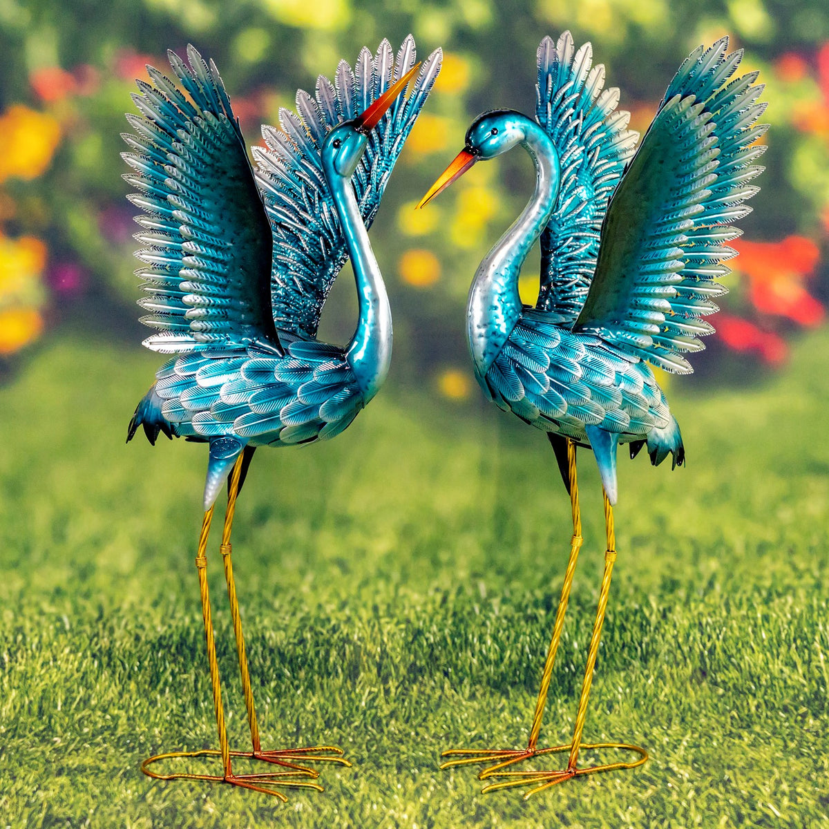 Pair of blue-green crane figurines standing on grass with wings raised