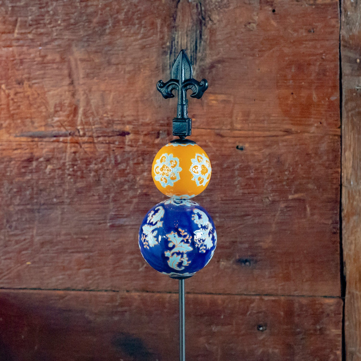 Orange and cobalt blue floral ceramic spheres on an iron garden stake