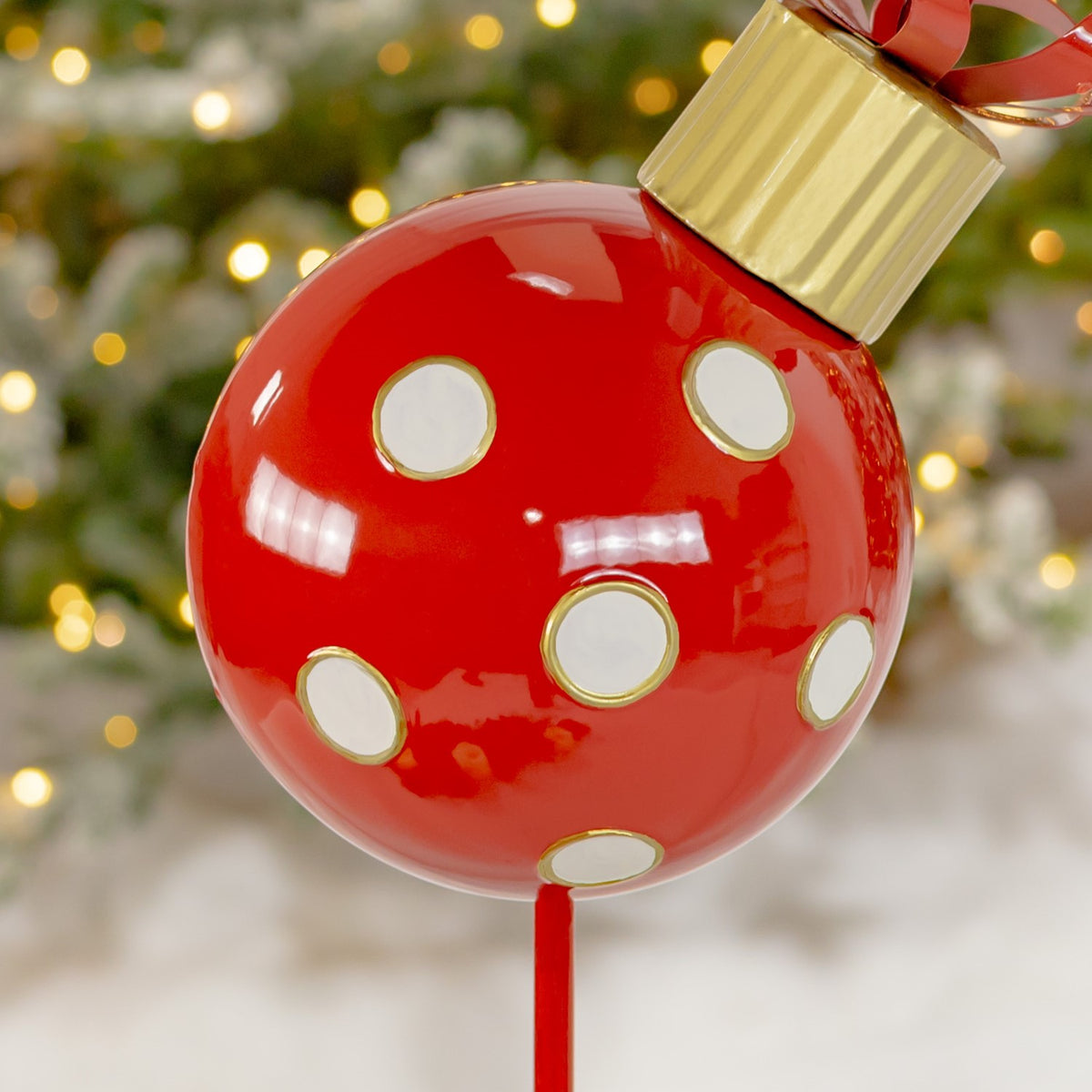 Close-up of white circular dots with gold rims on the glossy red ornament and its attached stake.