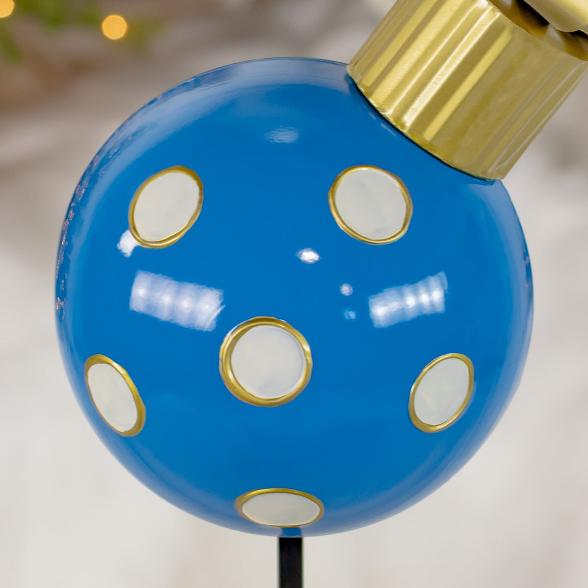 Close-up of white dots outlined in gold on the glossy blue ornament beneath its gold cap