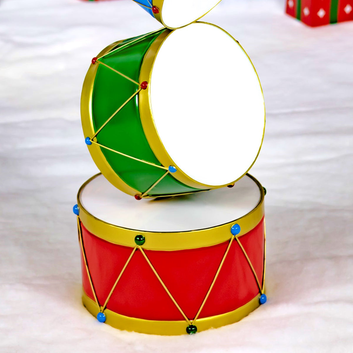 Close-up of a green drum above a red base drum, showing their gold trim and decorative cords.
