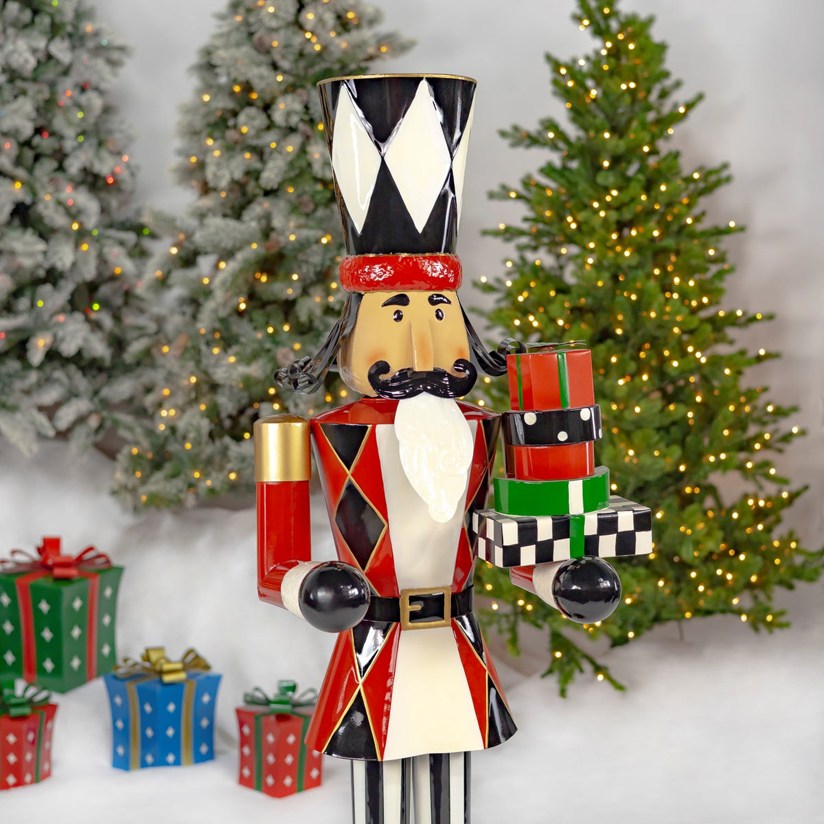 Angled view of the nutcracker holding a stack of colorful presents, with lit Christmas trees behind it.