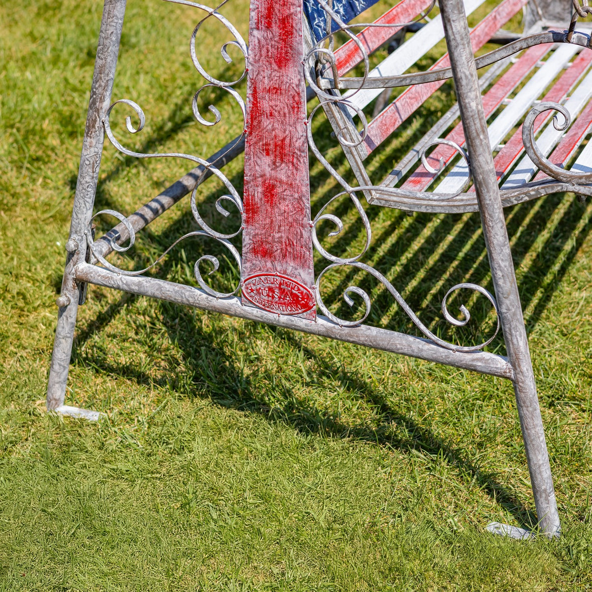 Detail of the swing bench's distressed red flag panel and iron base