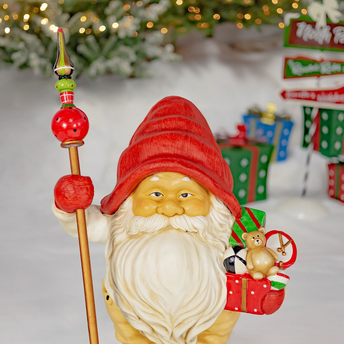 One Santa gnome holds a tall ornamented staff and a red gift decorated with a small reindeer.