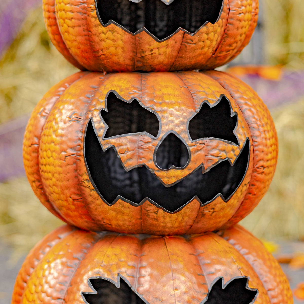 Close-up of two pumpkin faces with dark jagged eyes, noses, and mouths against textured orange surfaces.