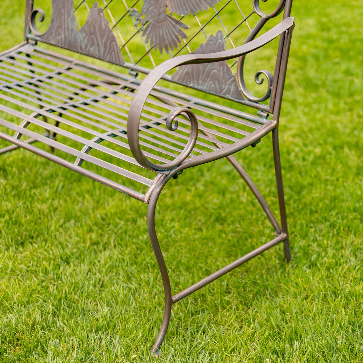 Close-up of a curled metal armrest, slatted seat, and curved bench leg on grass.