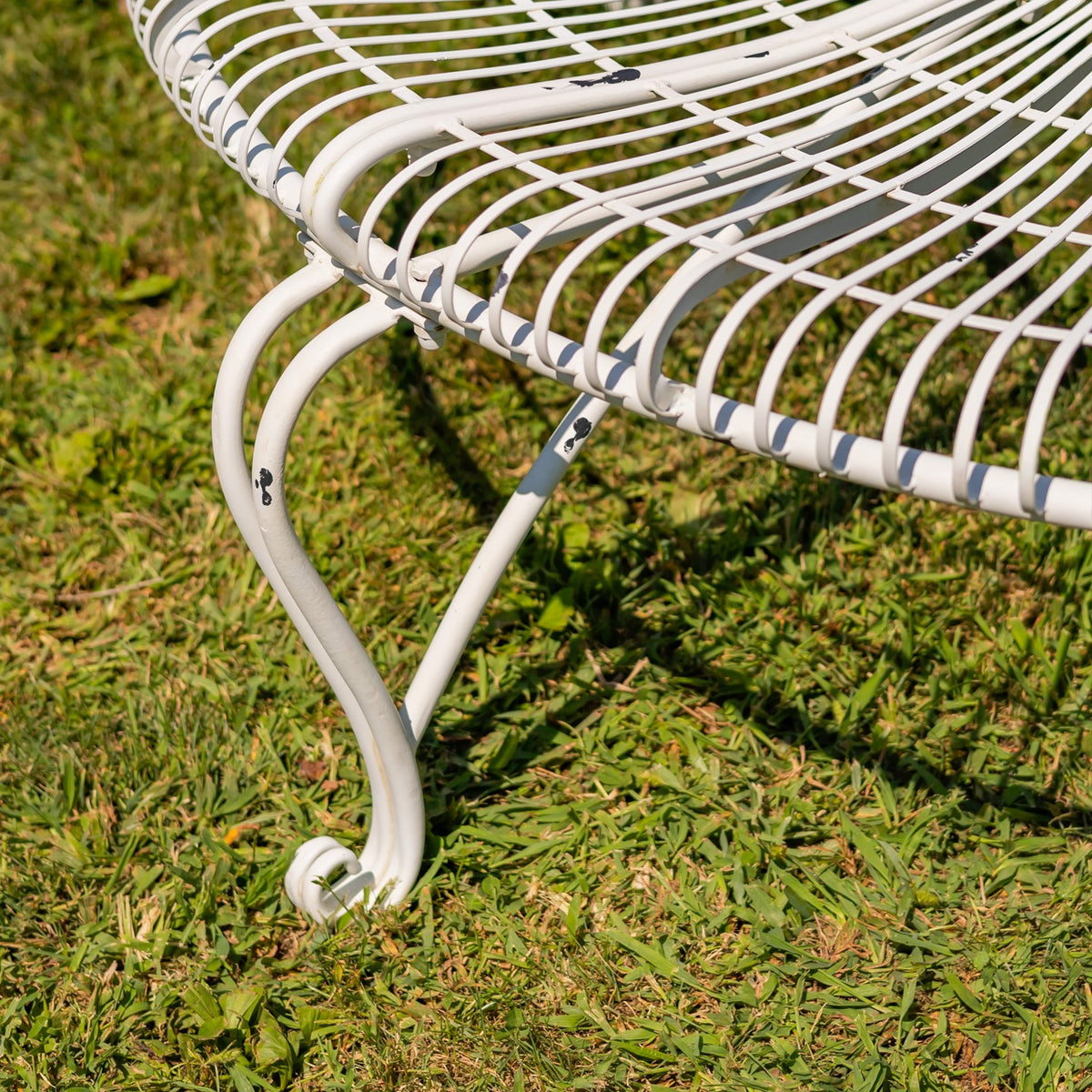 Curved white metal bench leg with a curled foot beneath the slatted seat.