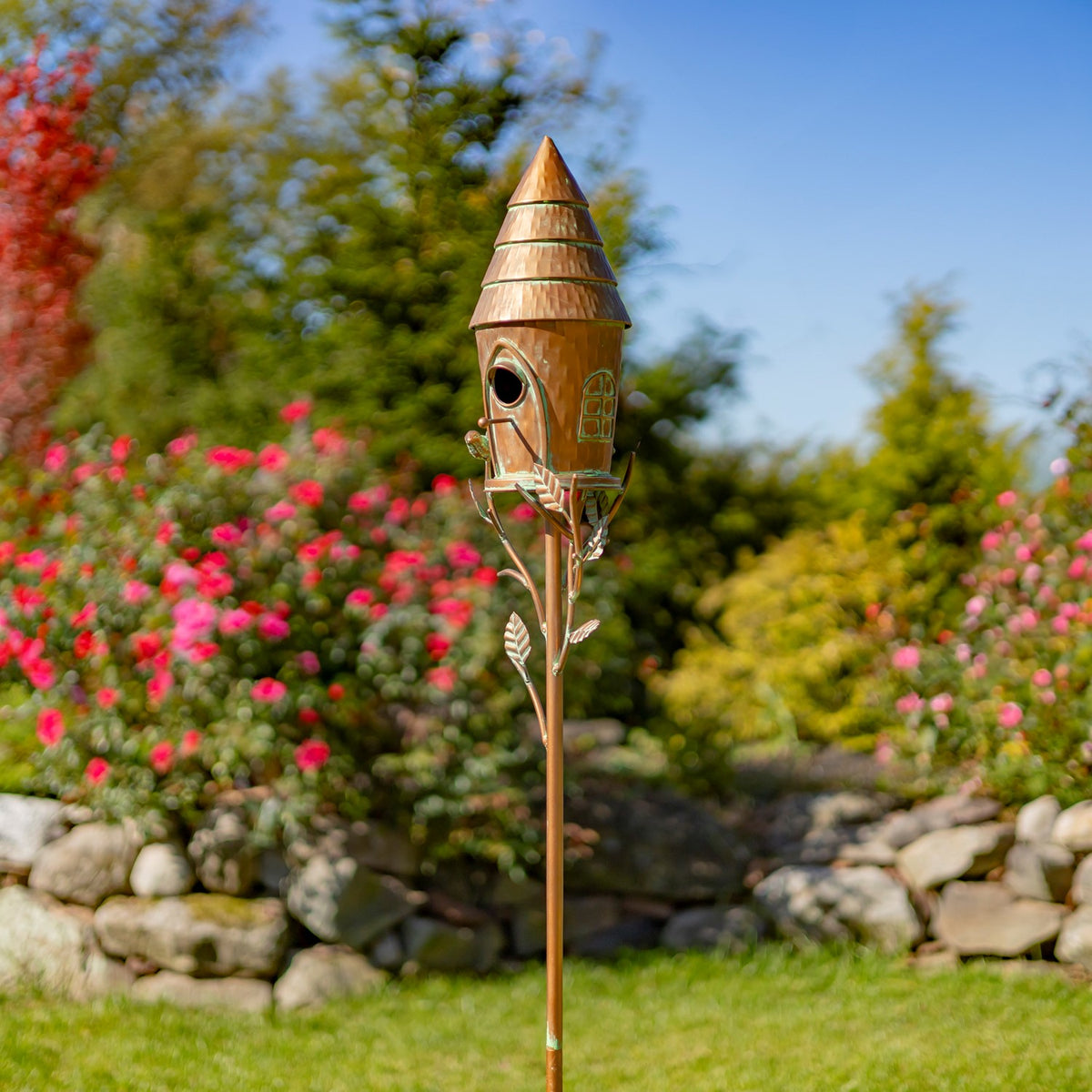 Copper birdhouse stake viewed at an angle among garden flowers