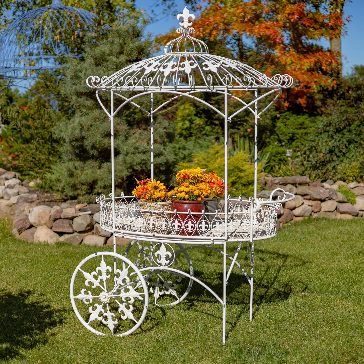 White ornate flower cart filled with colorful flowers on a lawn beneath a decorative canopy.