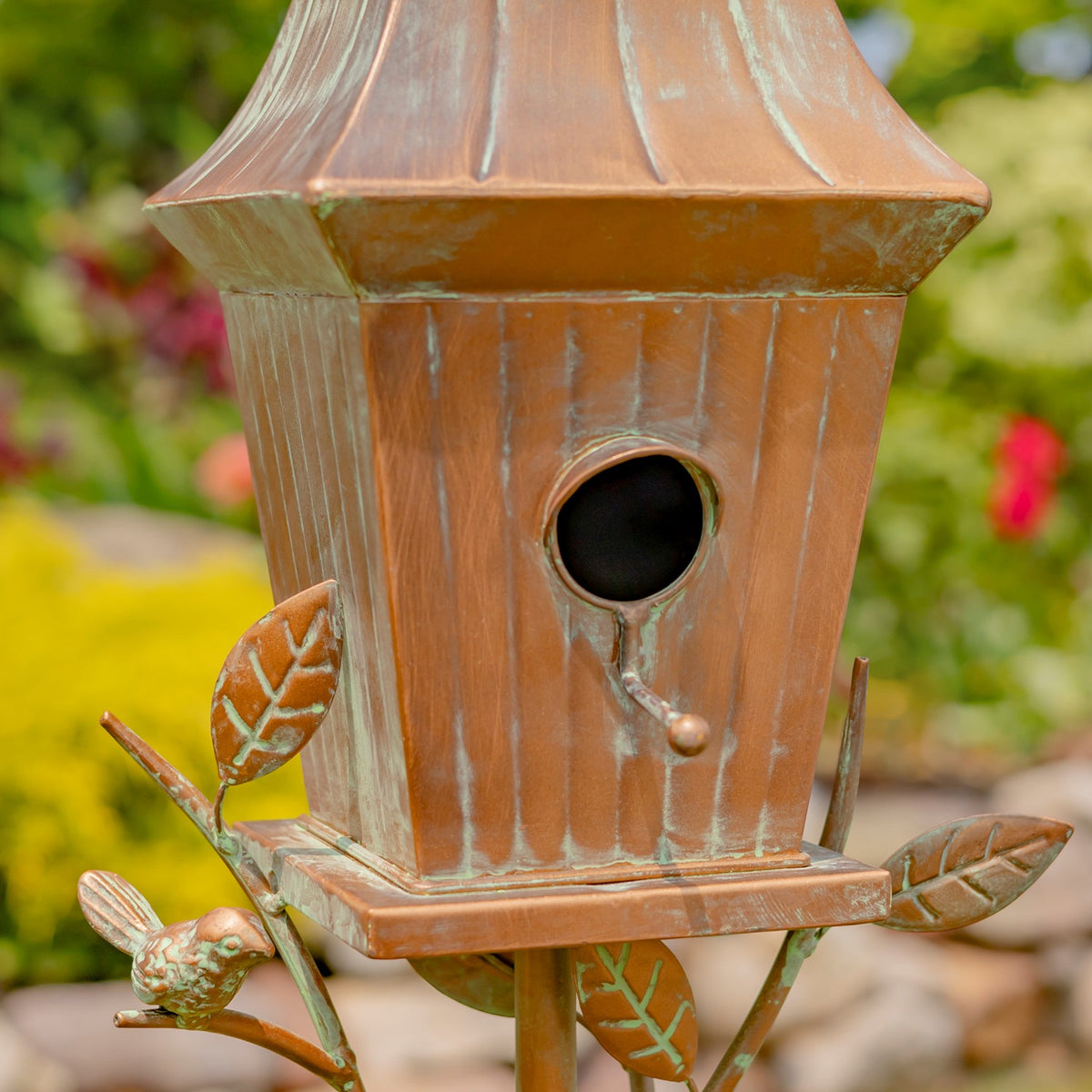 Close-up of the round birdhouse opening, small perch, and decorative bird and leaves.