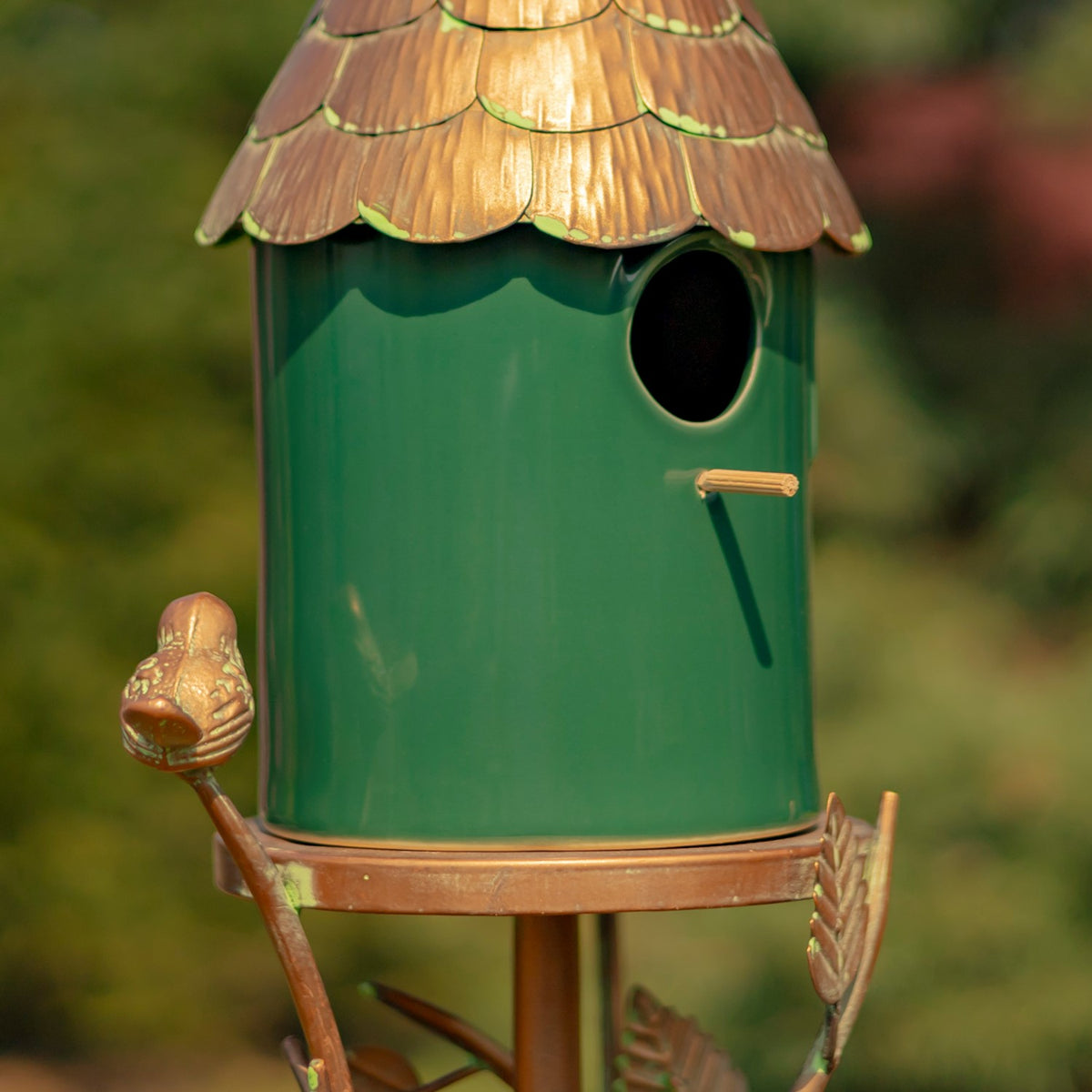 Close-up of the birdhouse entrance, green body, copper-colored perch and bird ornament on a branch.