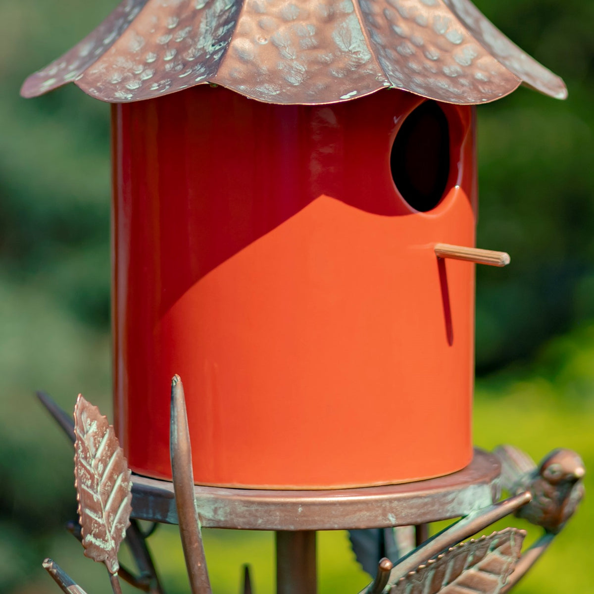Tight view of the birdhouse entrance and perch above a metal tray decorated with leaf and bird shapes.