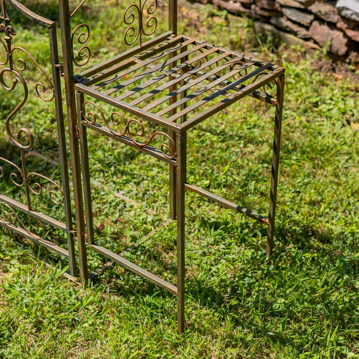 Close-up of a narrow metal plant stand with a slatted top beside the archway, set over grass.