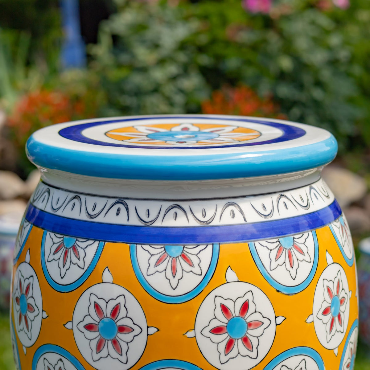 Close view of the stool’s blue-edged top and yellow body with repeating white floral motifs.
