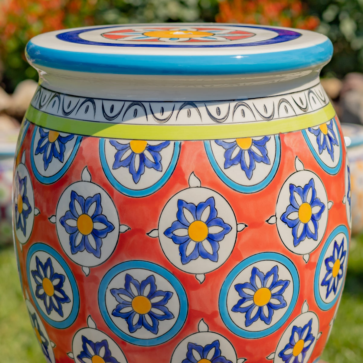 Close-up of the coral ceramic body with repeating blue-and-yellow flowers and a patterned rim.