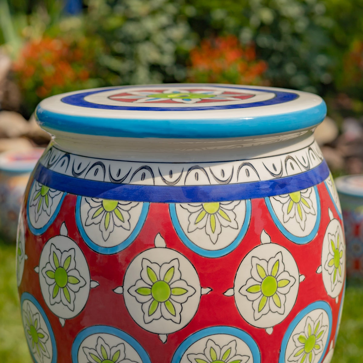 Close view of the stool’s blue-edged top and red body, decorated with repeating white floral medallions.