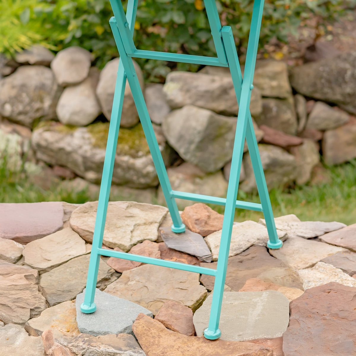 Close view of the turquoise crossed legs, support bars, and rounded feet on stone paving.
