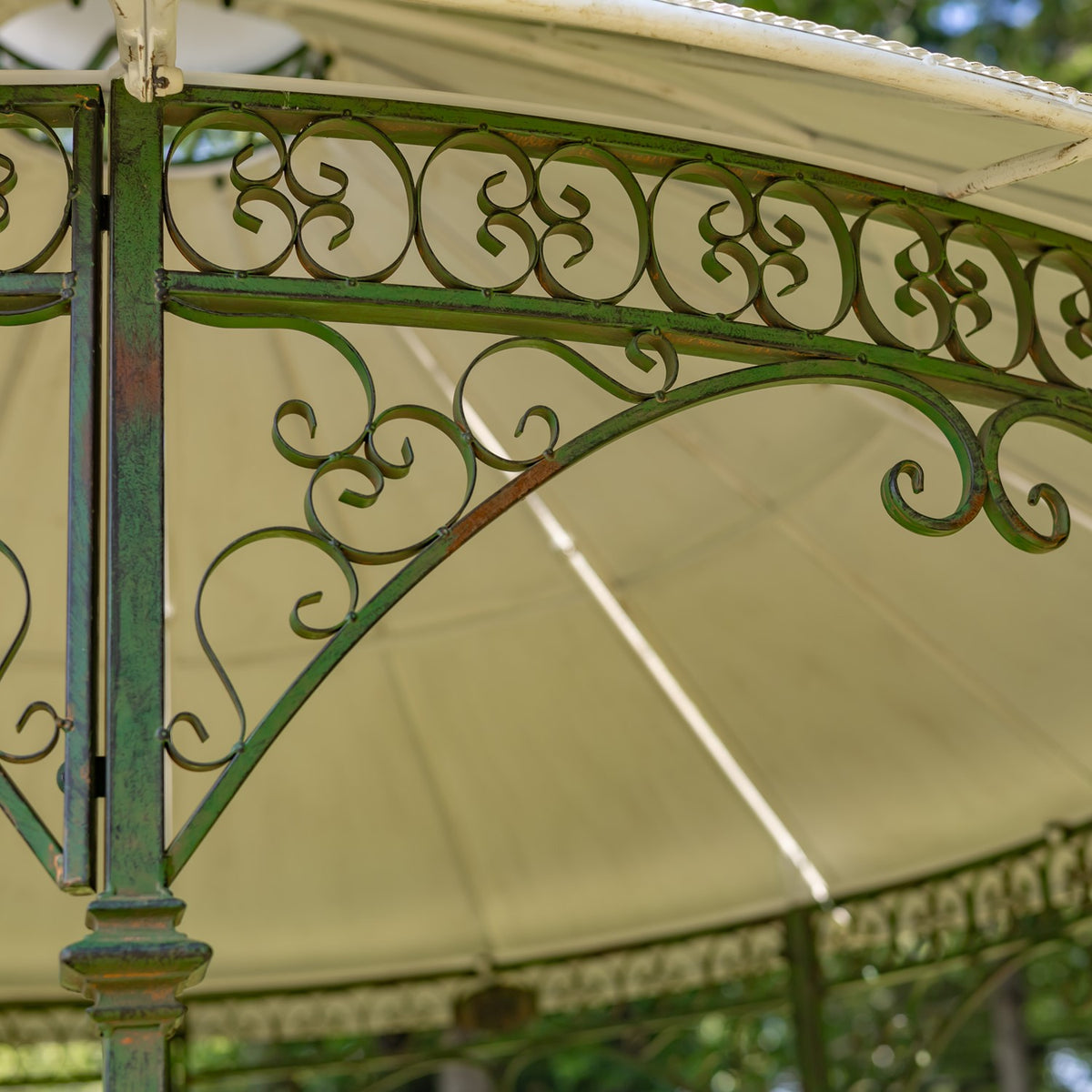 Close-up of a green gazebo post and ornate scrollwork beneath the pale canopy.