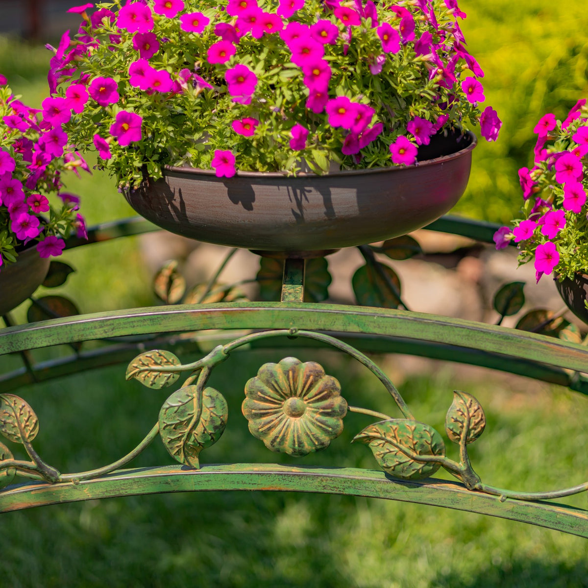 A dark bowl planter overflowing with pink flowers, framed by a central metal flower ornament.