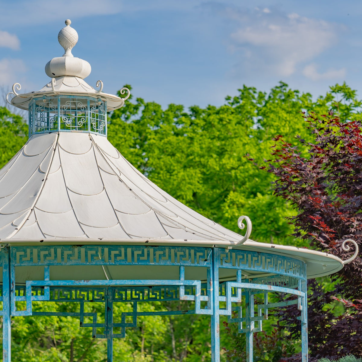 Angled close-up of the gazebo's pale roof, ornamental finial and scrollwork along the roof edge.