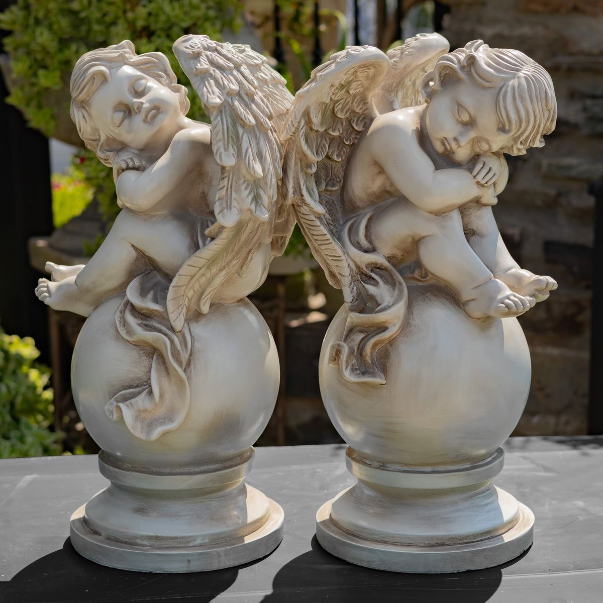 Two antique-finish cherub statues on globe pedestals viewed from the side