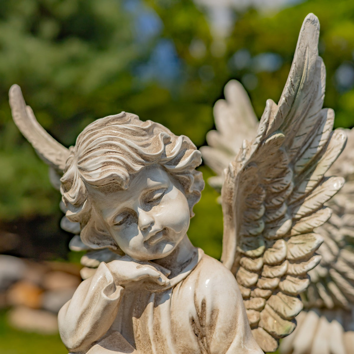 Close-up of a cherub's face and detailed wings against garden greenery