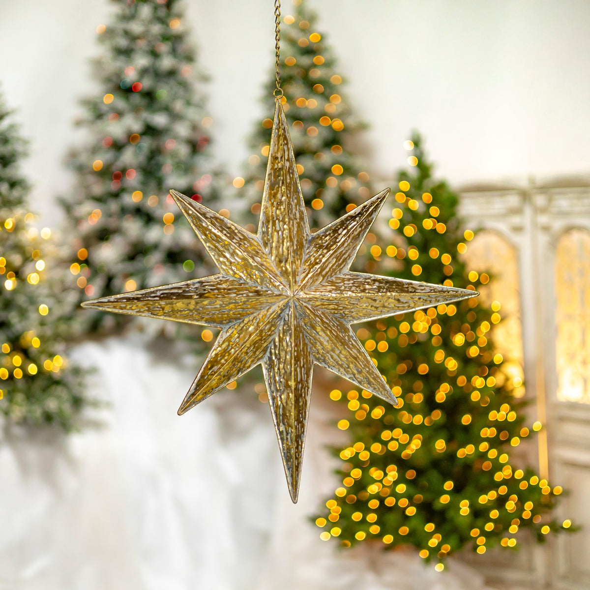 A hanging gold star is shown at an angle, with a lit tree and decorative screen behind it.
