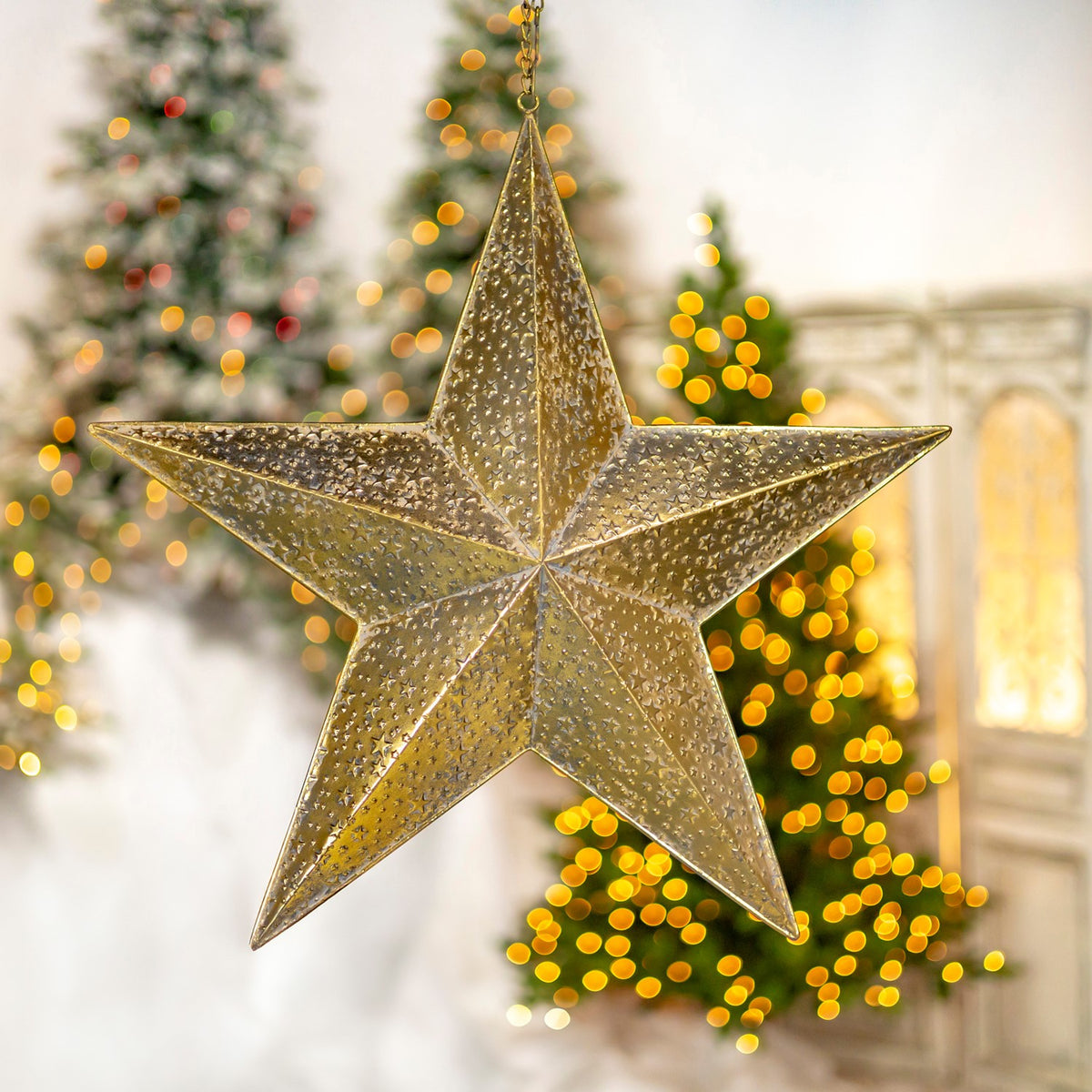 A hanging gold five-point star is shown against a Christmas tree and a warm-lit cabinet.