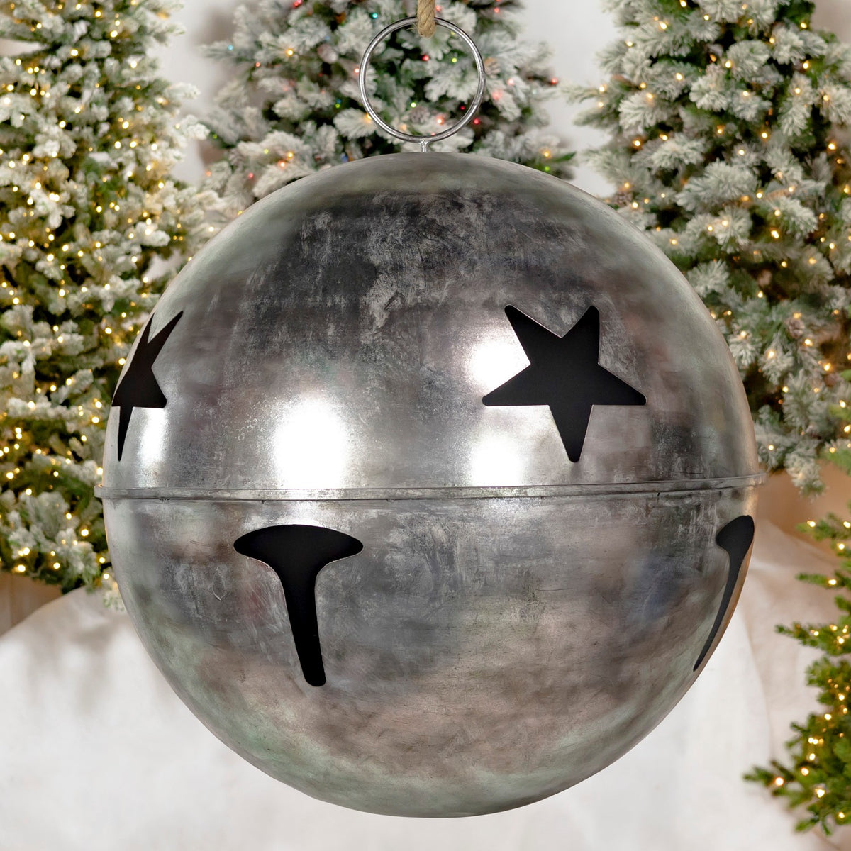Close view of a large silver bell with star cutouts, a seam around its middle, and a hanging ring.