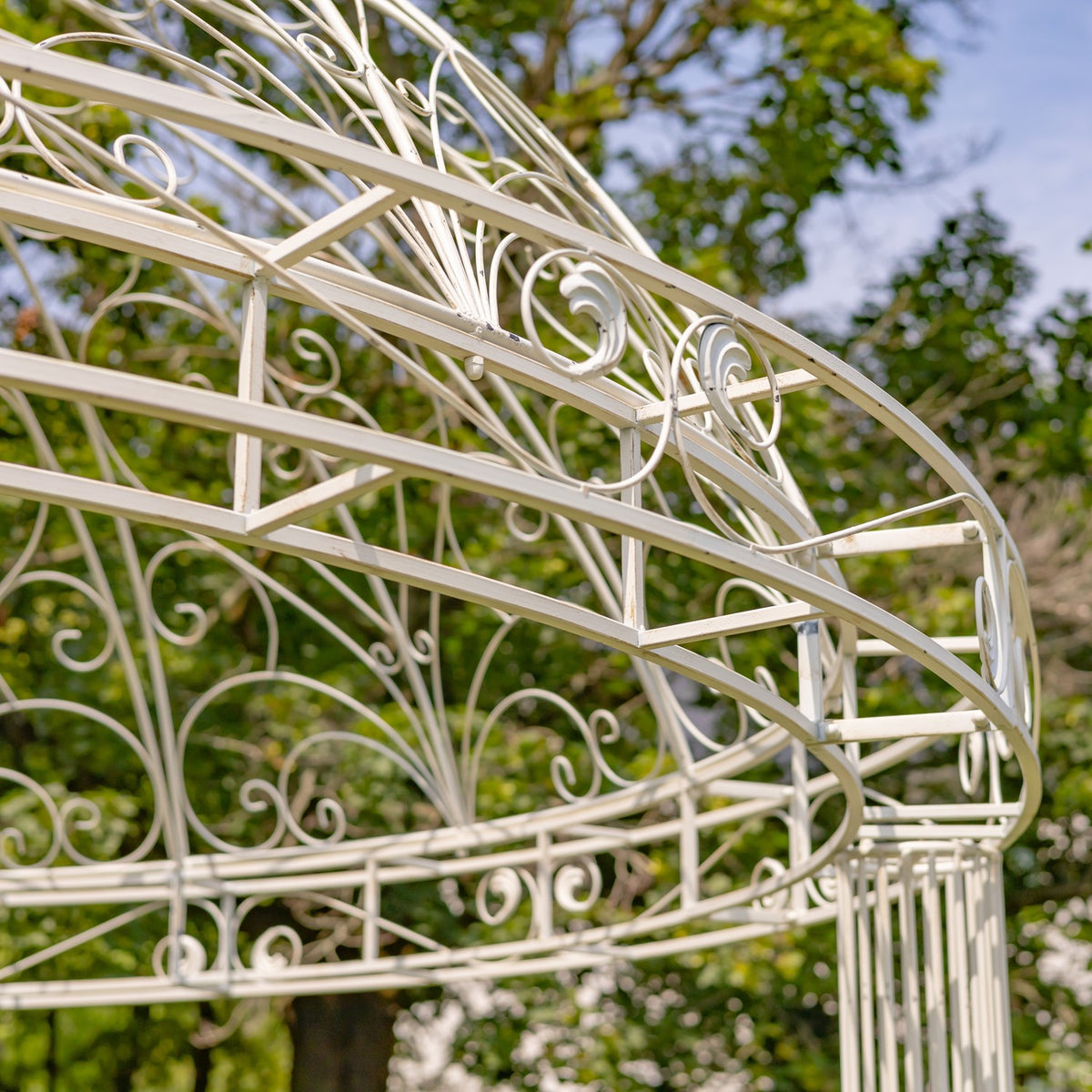 Angled view of the gazebo’s curved roof frame, ornate scrollwork, and supporting iron bars.