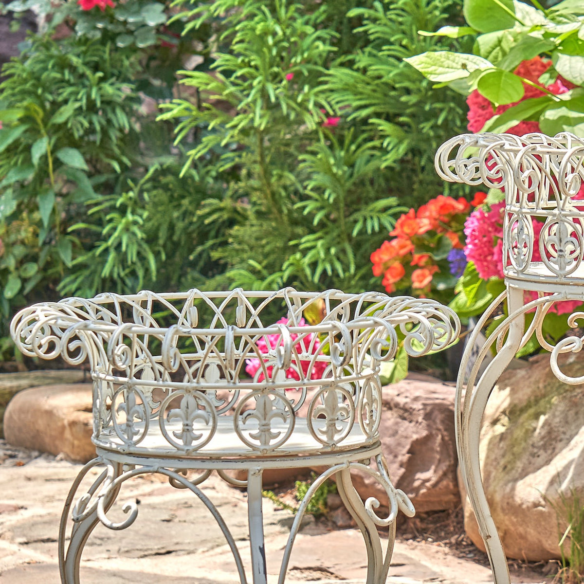 Close view of an ornate cream-colored metal plant stand with a round basket and curled decorative legs.